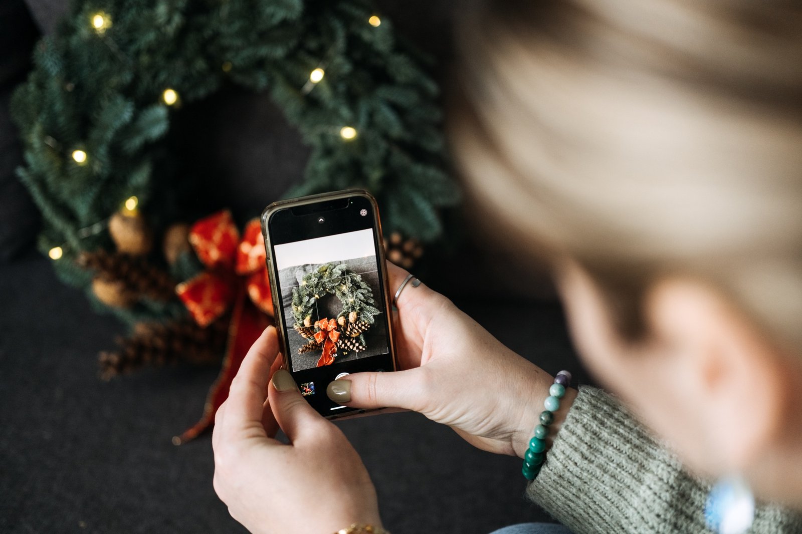 Woman photographing black cat with Christmas wreath and lights for social media content. Festive